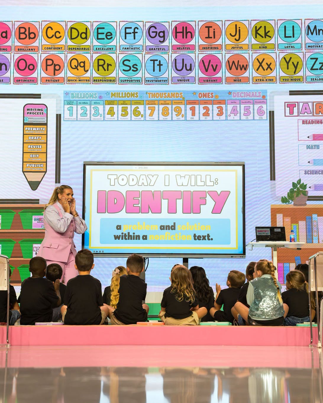 A presenter teaching a nonfiction reading lesson to elementary students seated on a classroom stage set at a Get Your Teach On event